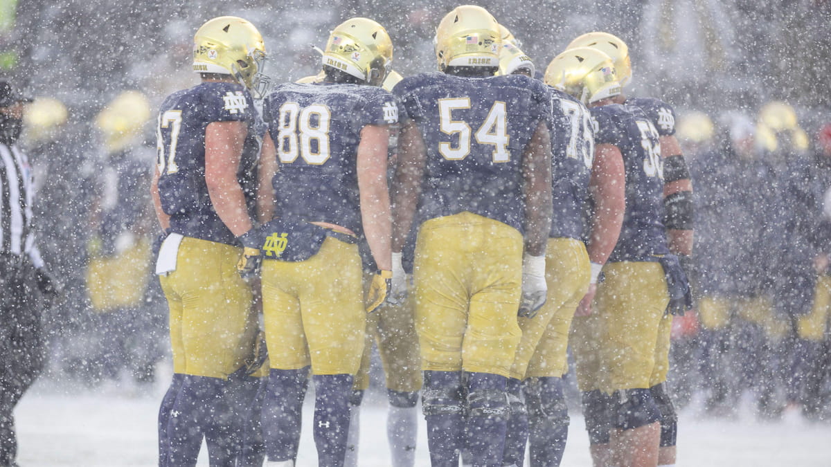 Notre Dame football players huddle in the snow.