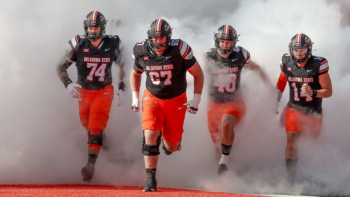 Oklahoma State players run onto the field on a hot day.